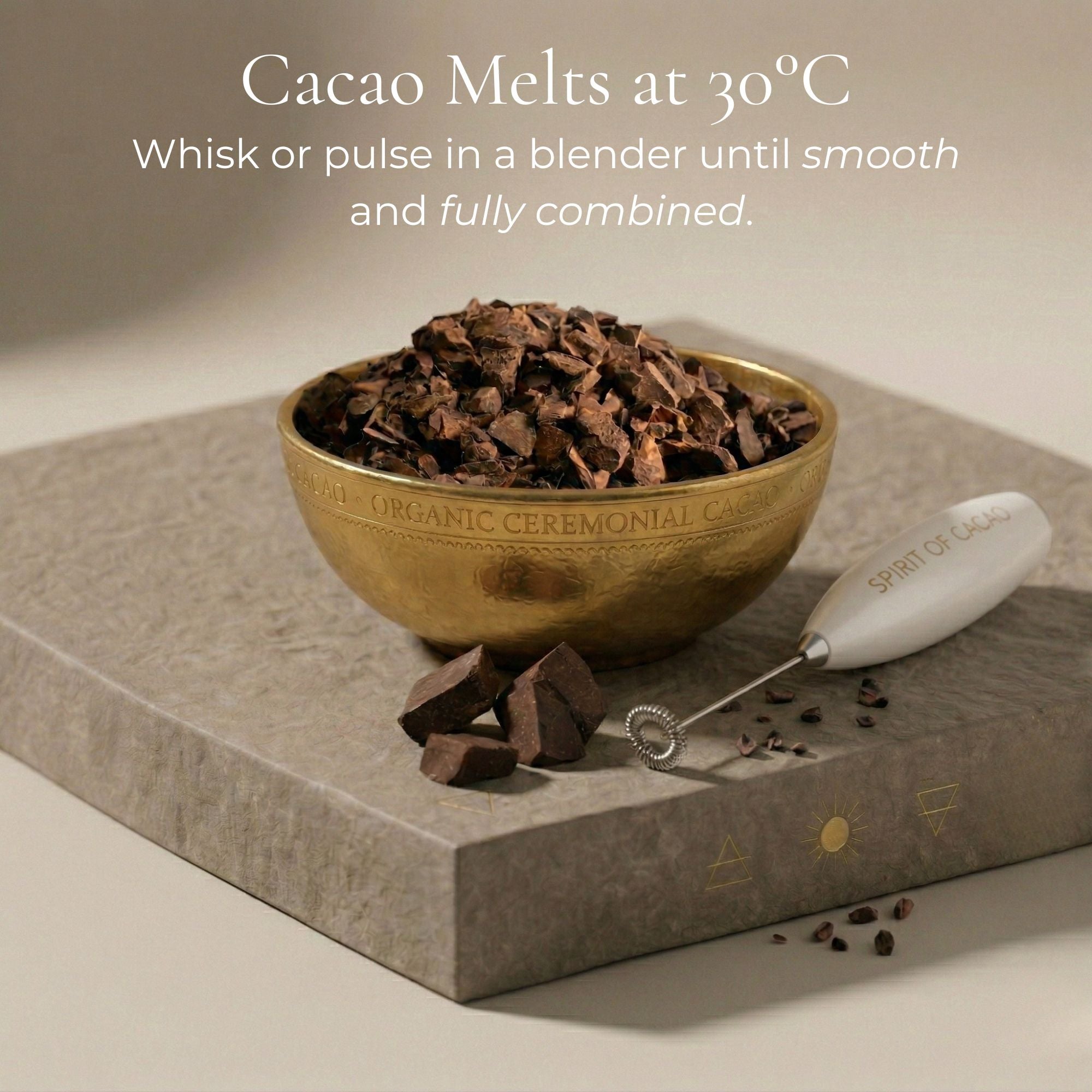 Bowl of cacao melts with a whisk on a stone surface, featuring branding.