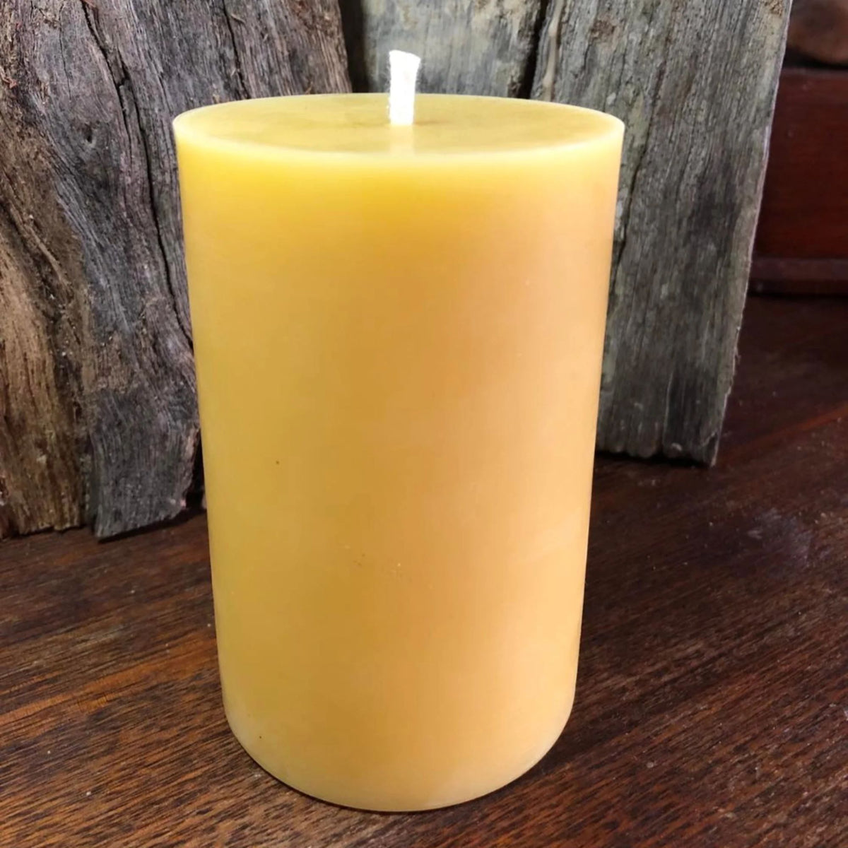 Yellow natural 100% beeswax candle on a wooden surface with a rustic background