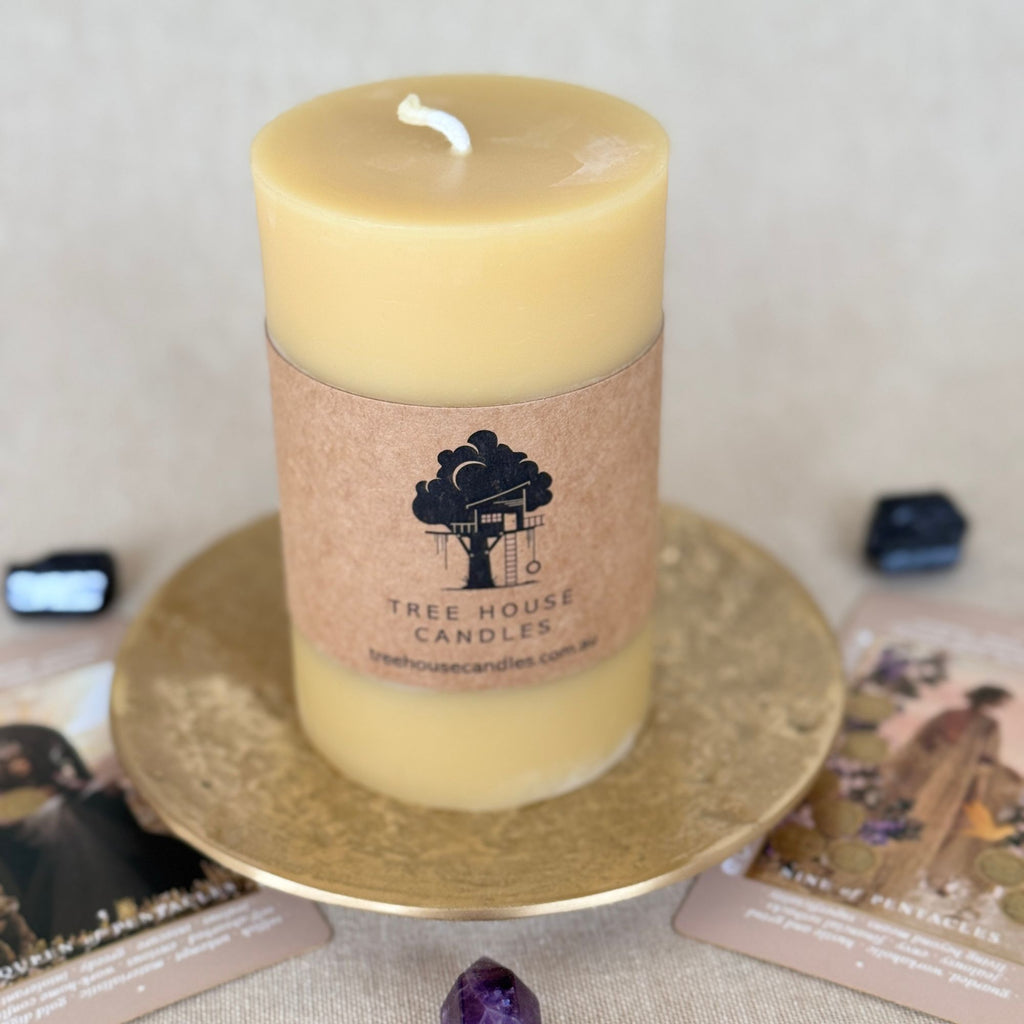 Yellow 100% pure beeswax candle with a label on a decorative plate, surrounded by books and crystals making it the perfect ritual or magic metaphysical item for long ceremonies or rituals