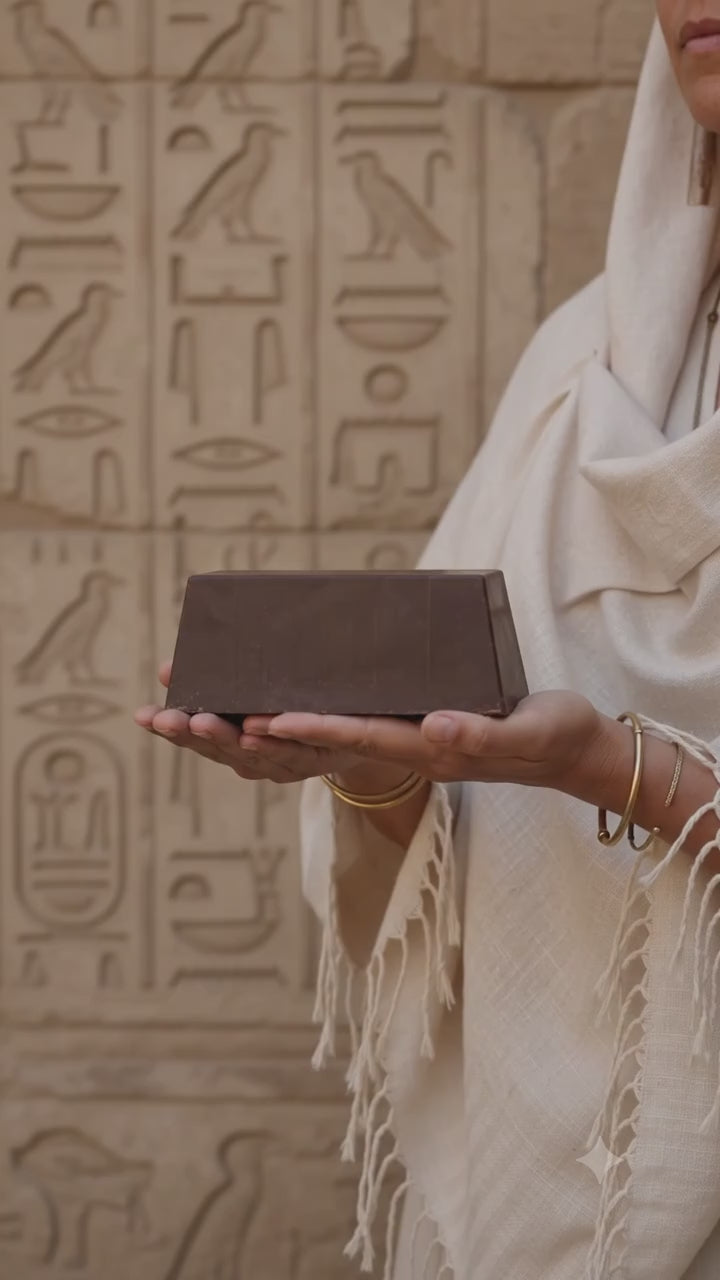 female holding 600g ceremonial cacao block in egypt in front of hieroglyphs, rotating the 600g block to show case each side.